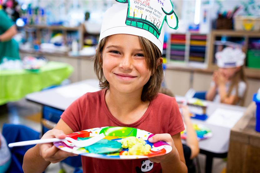 A brown-haired girl holds up a plate with eggs and ham